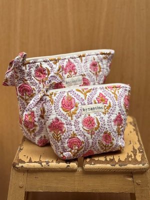 Duo de trousses beauté Byzantine à fleurs roses sur fond lilas pâle, posées sur un tabouret