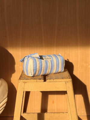 Trousse à crayons Byzantine rayée bleu ciel et écru posée sur un tabouret en bois