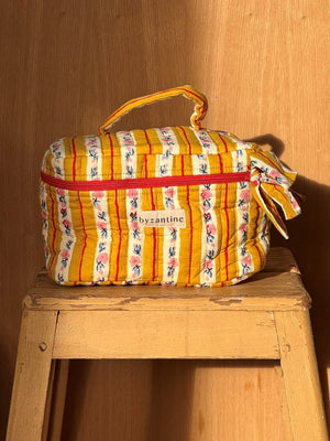 Trousse vanity Byzantine à rayures moutarde, rouges et fleuries, avec poignée, sur un tabouret