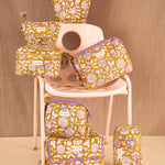 Collection de trousses Carthage Kaki de Byzantine, fleurs lilas sur fond kaki, sur une chaise rose