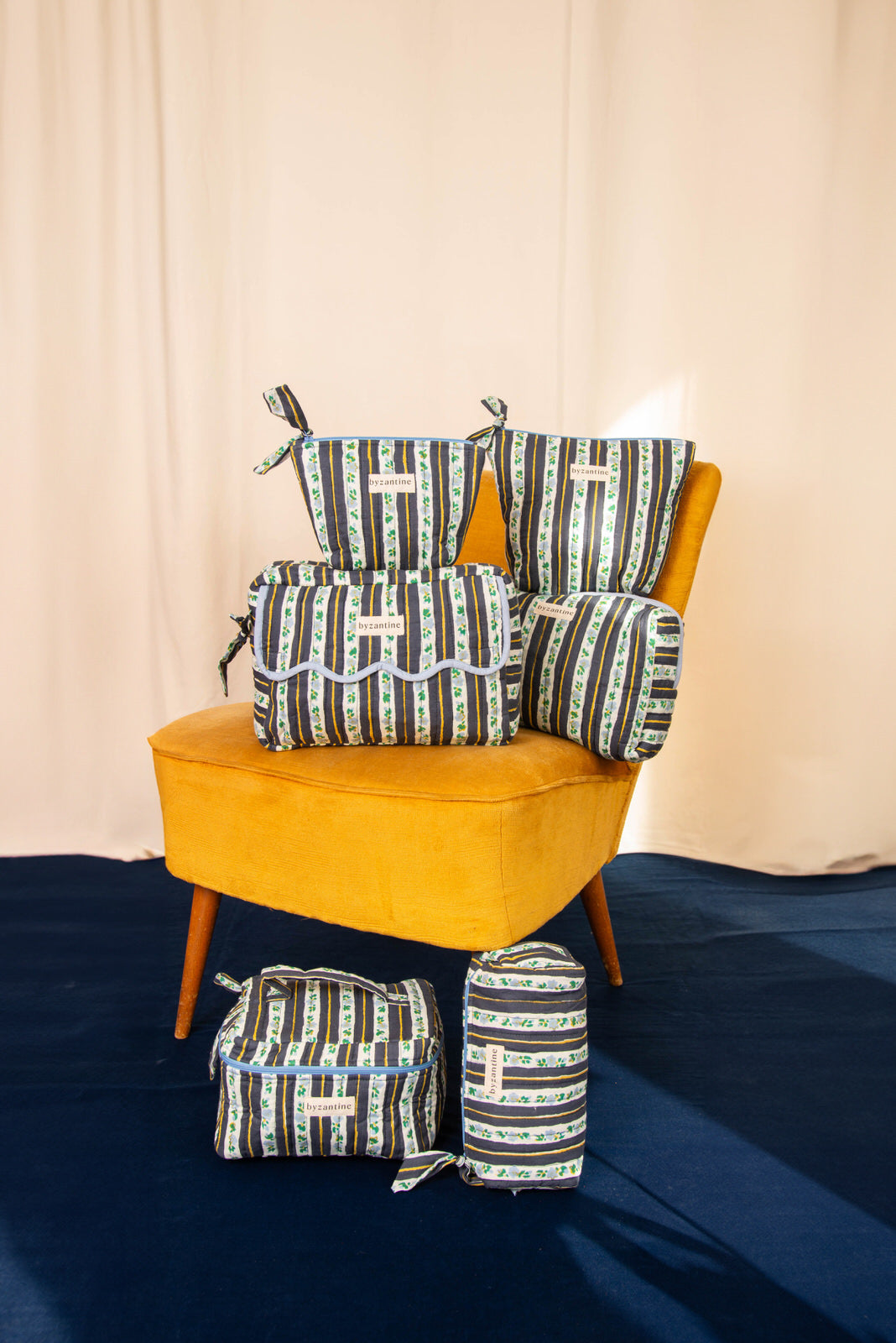 Collection de trousses Flora Bleu marine de Byzantine, rayures fleuries, sur un fauteuil moutarde