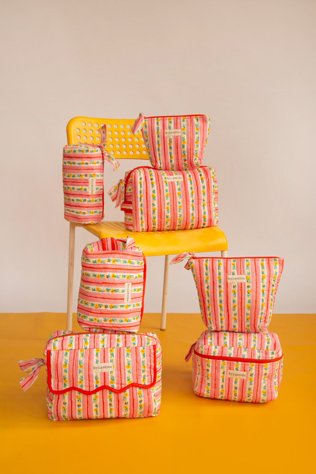 Collection de trousses Flora Rose de Byzantine, rayures fleuries rose et rouge, sur une chaise jaune