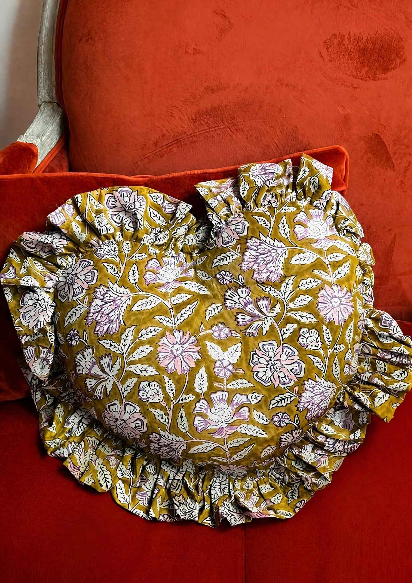 Coussin cœur Carthage Kaki de byzantine, imprimé fleuri kaki et blanc à volants, sur un canapé rouge