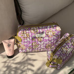 Trousses de toilette Carthage Lilas posées sur un banc avec une crème pour les mains