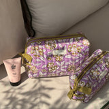 Trousses de toilette Carthage Lilas posées sur un banc avec une crème pour les mains