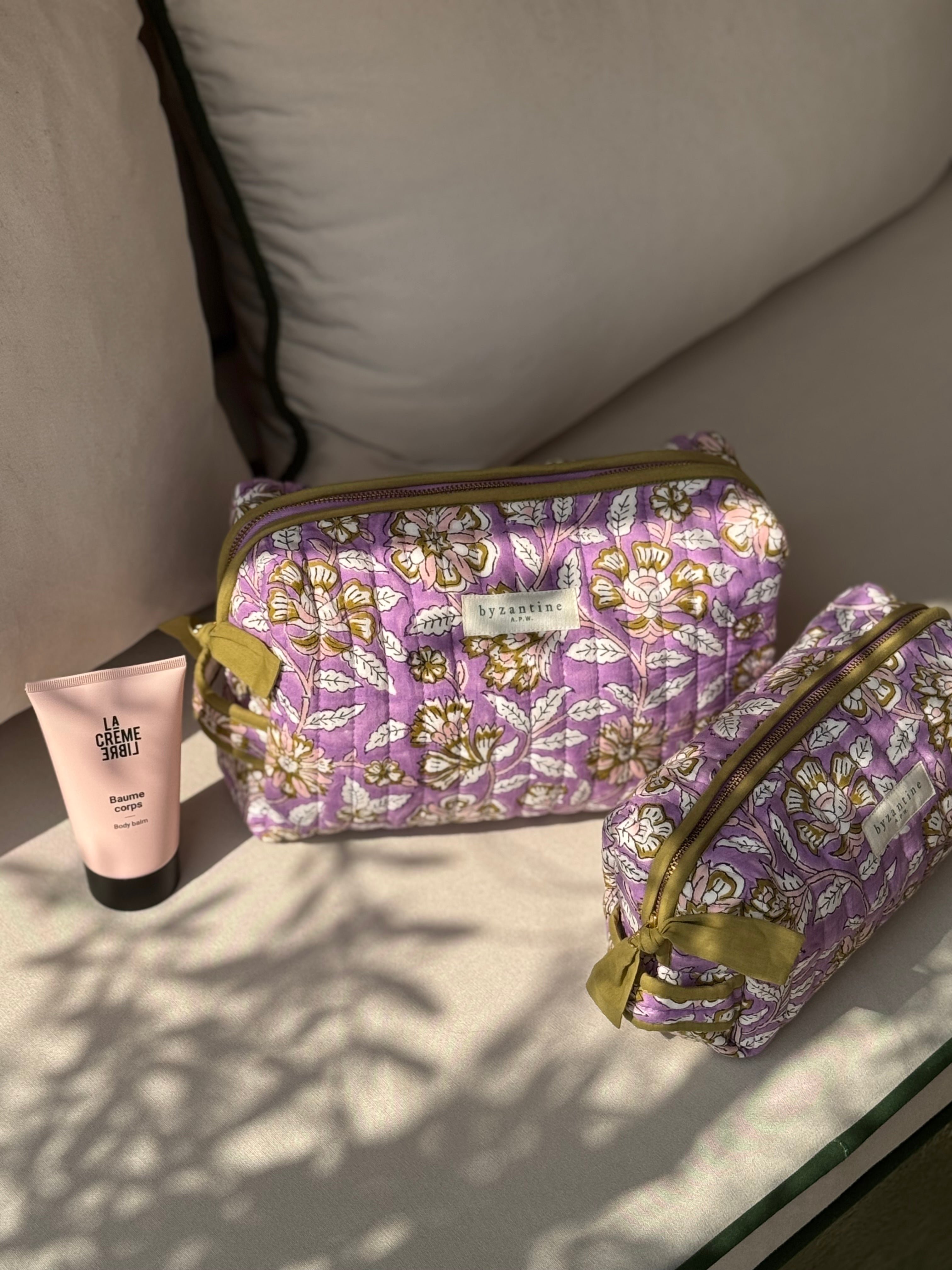 Trousses de toilette Carthage Lilas posées sur un banc avec une crème pour les mains