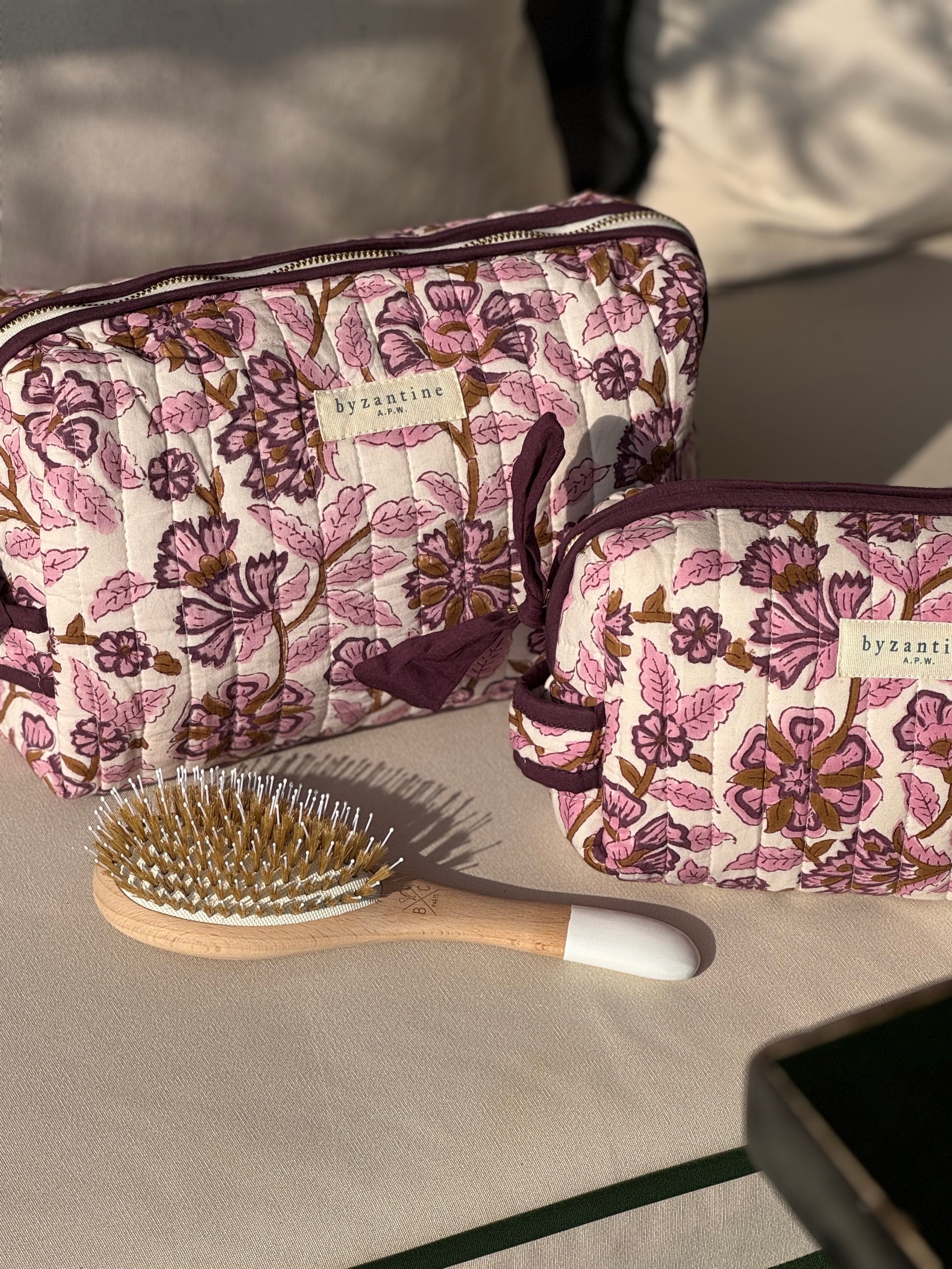 Trousses de toilette Carthage Prune posées sur un coussin, avec une brosse à cheveux