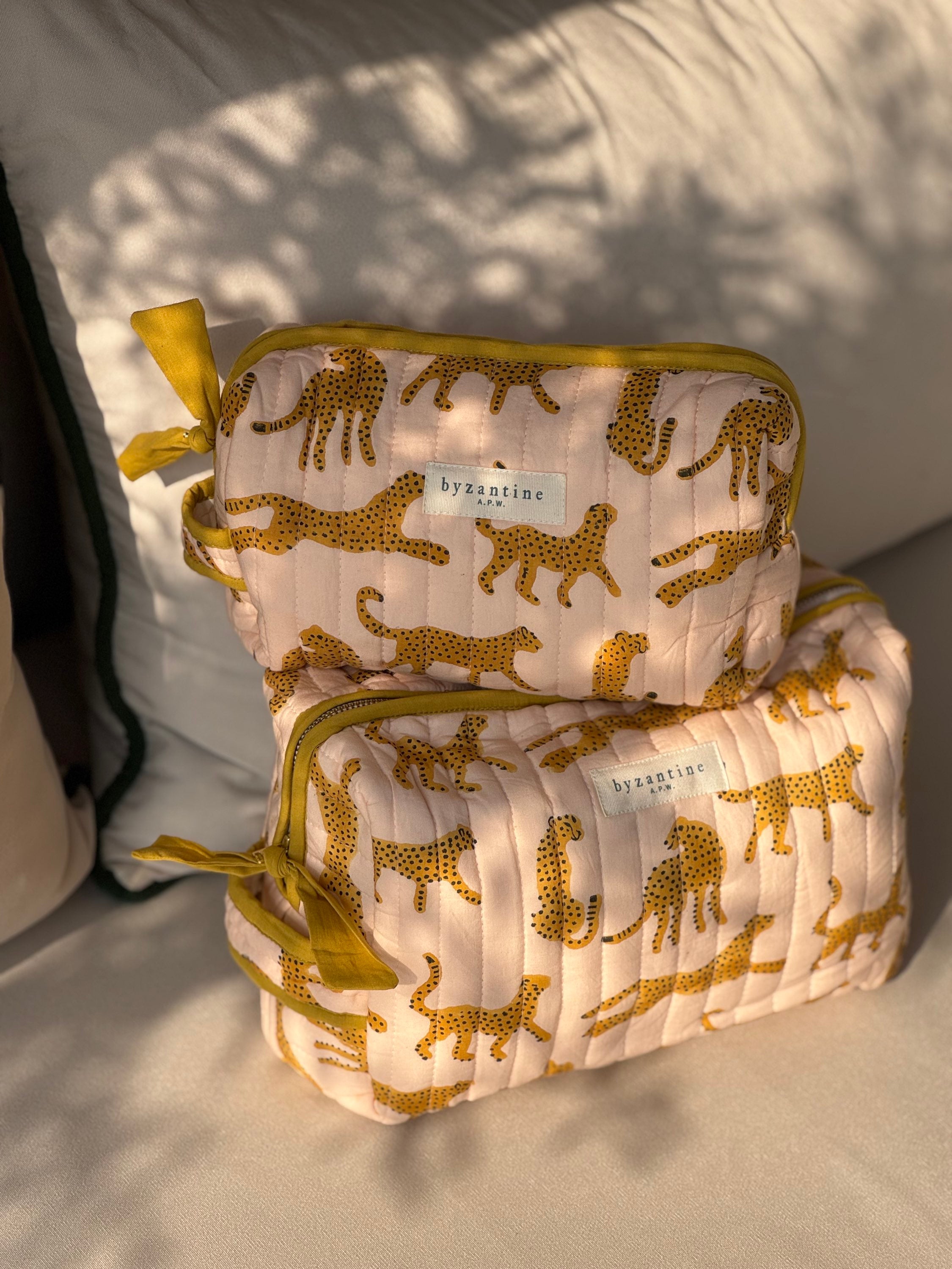 Grande et petite trousses de toilette Fauve Rose posées sur un coussin