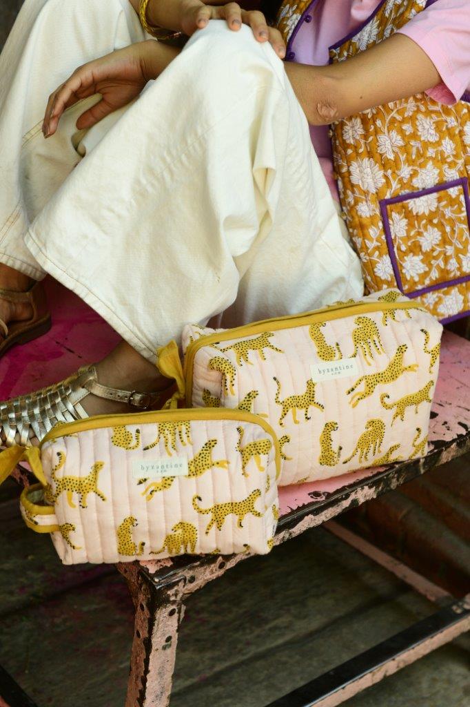 Trousses de toilette Fauve Rose de byzantine posées sur un banc à côté d'une femme assise