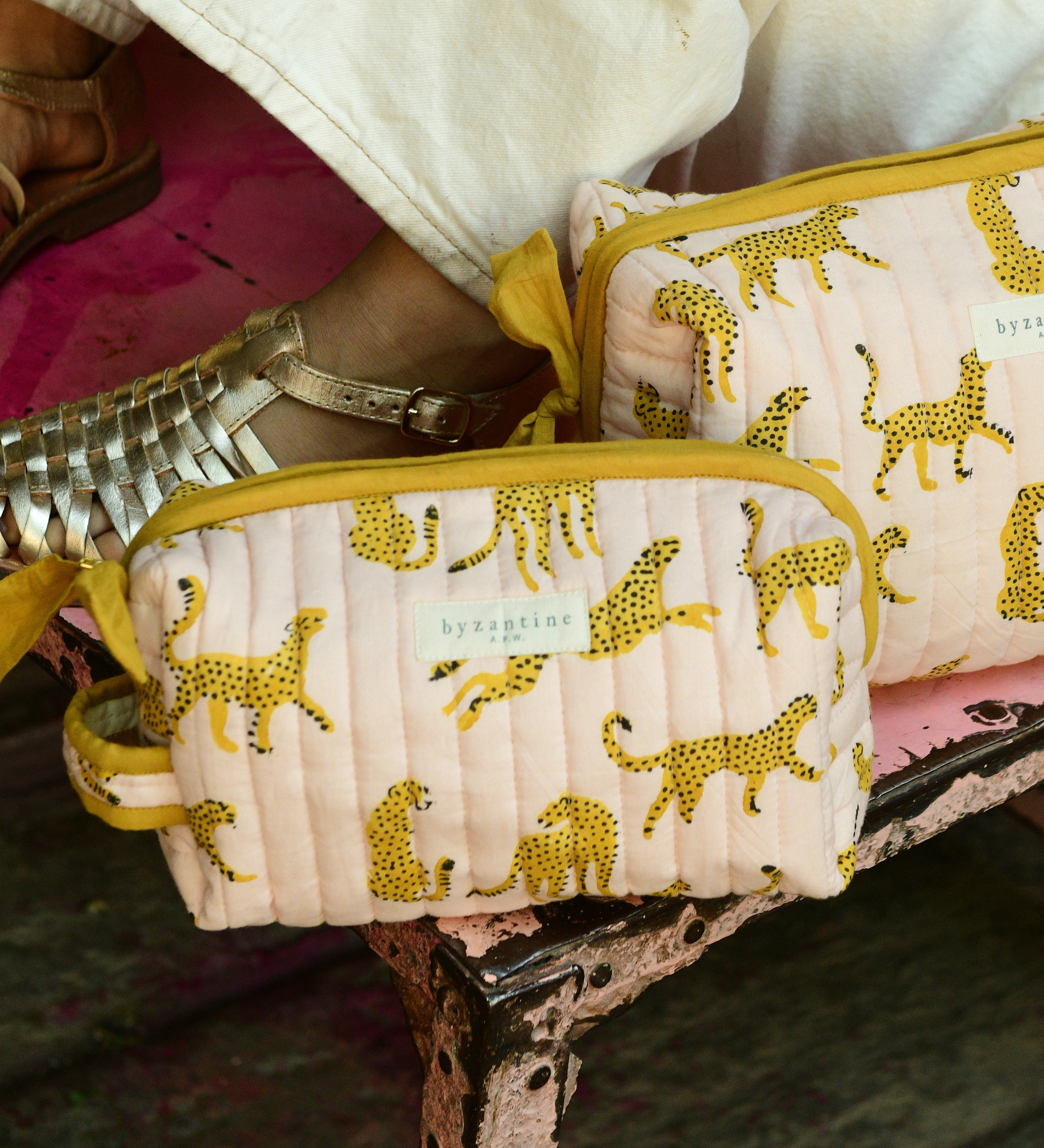 Duo de trousses de toilette Fauve Rose posées sur un banc, à motif guépards