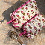 Trousses de toilette N°50 Rose posées sur un tapis, avec une brosse à cheveux
