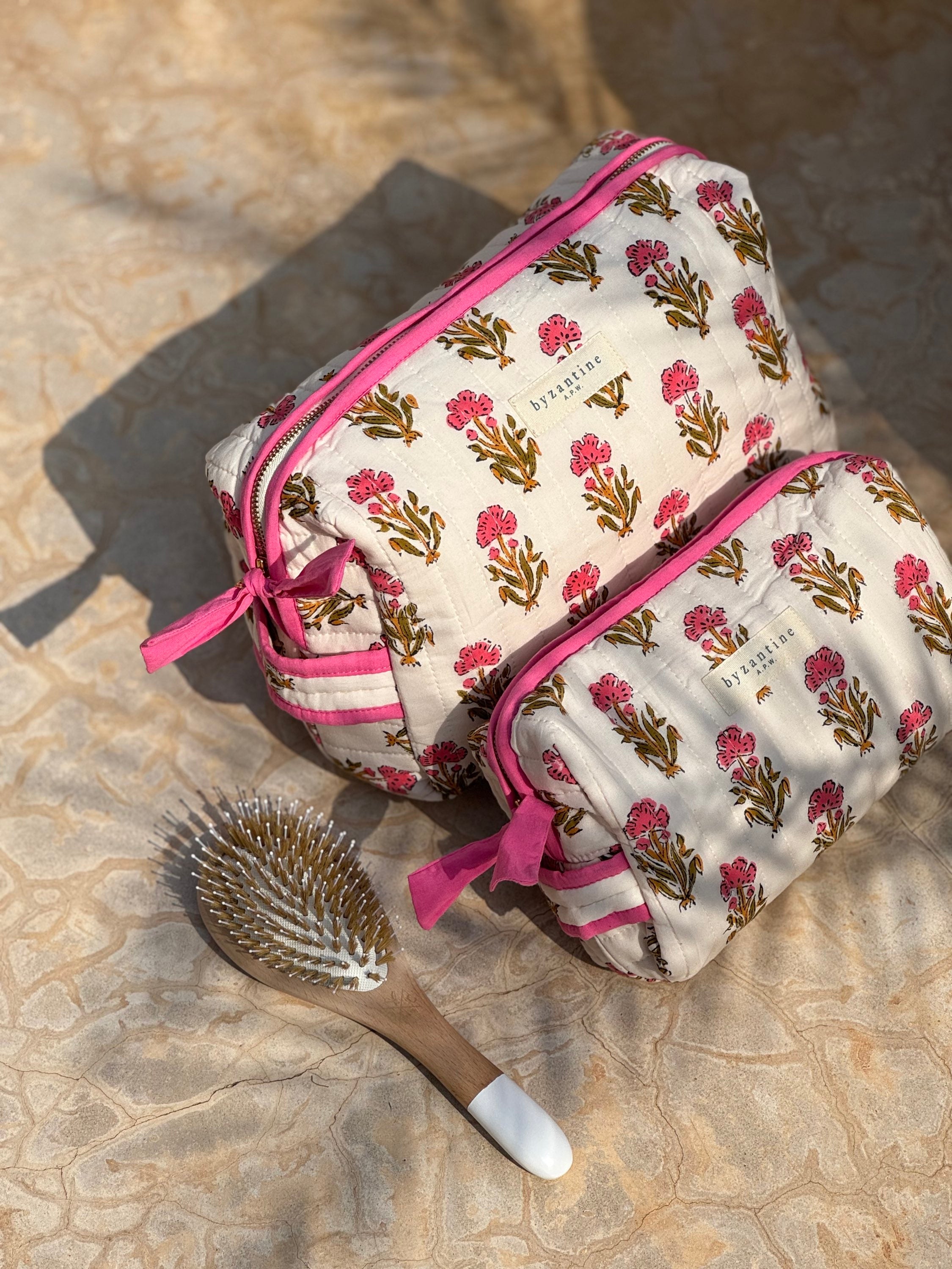 Trousses de toilette N°50 Rose posées sur un tapis, avec une brosse à cheveux