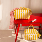 Trousse volants sur une table rouge et trousse vanity au sol, rayures Pacha Passion