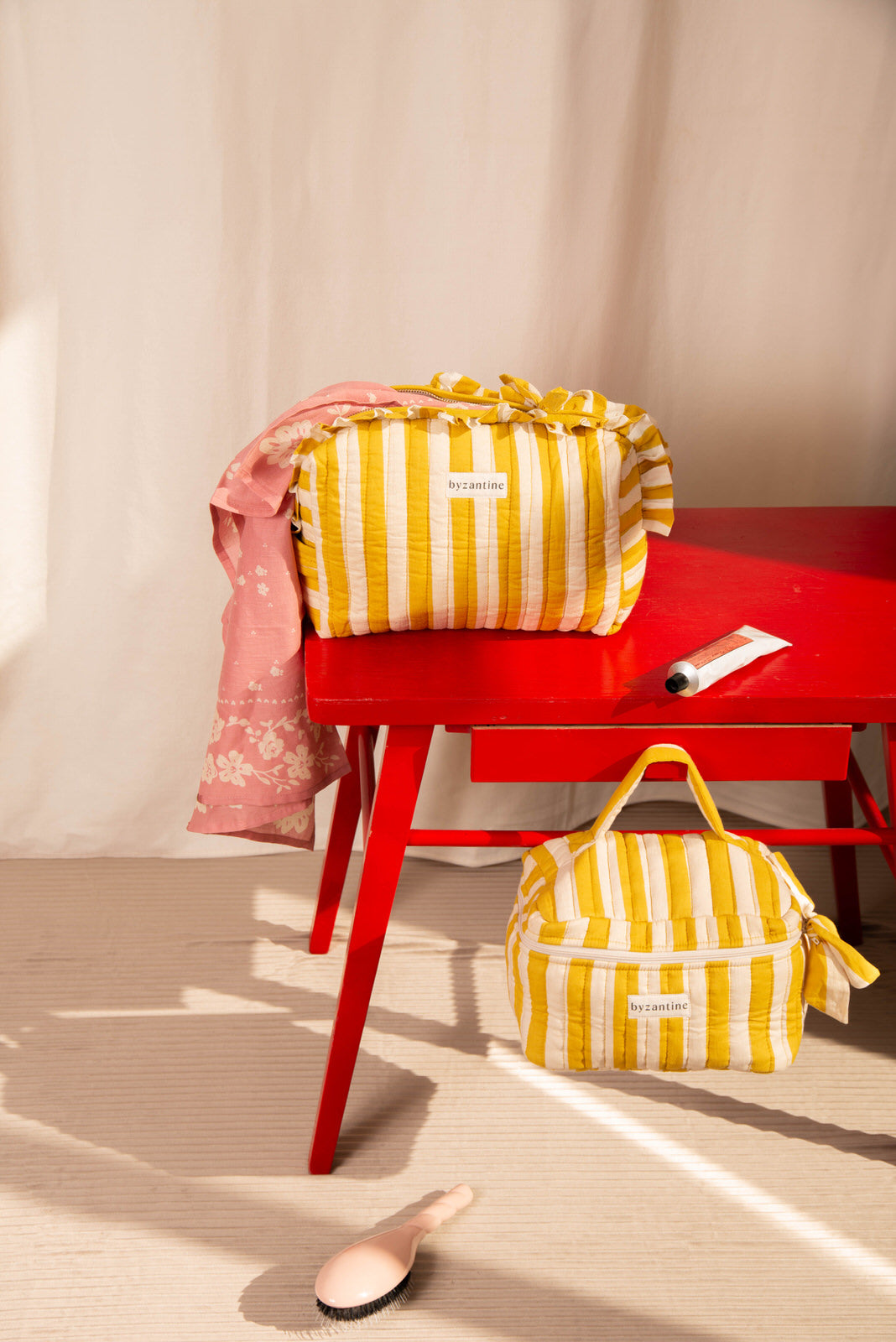 Trousse volants sur une table rouge et trousse vanity au sol, rayures Pacha Passion
