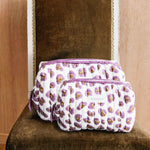 Duo de trousses de toilette Léopard Écru et Violet de byzantine posées sur une chaise en velours