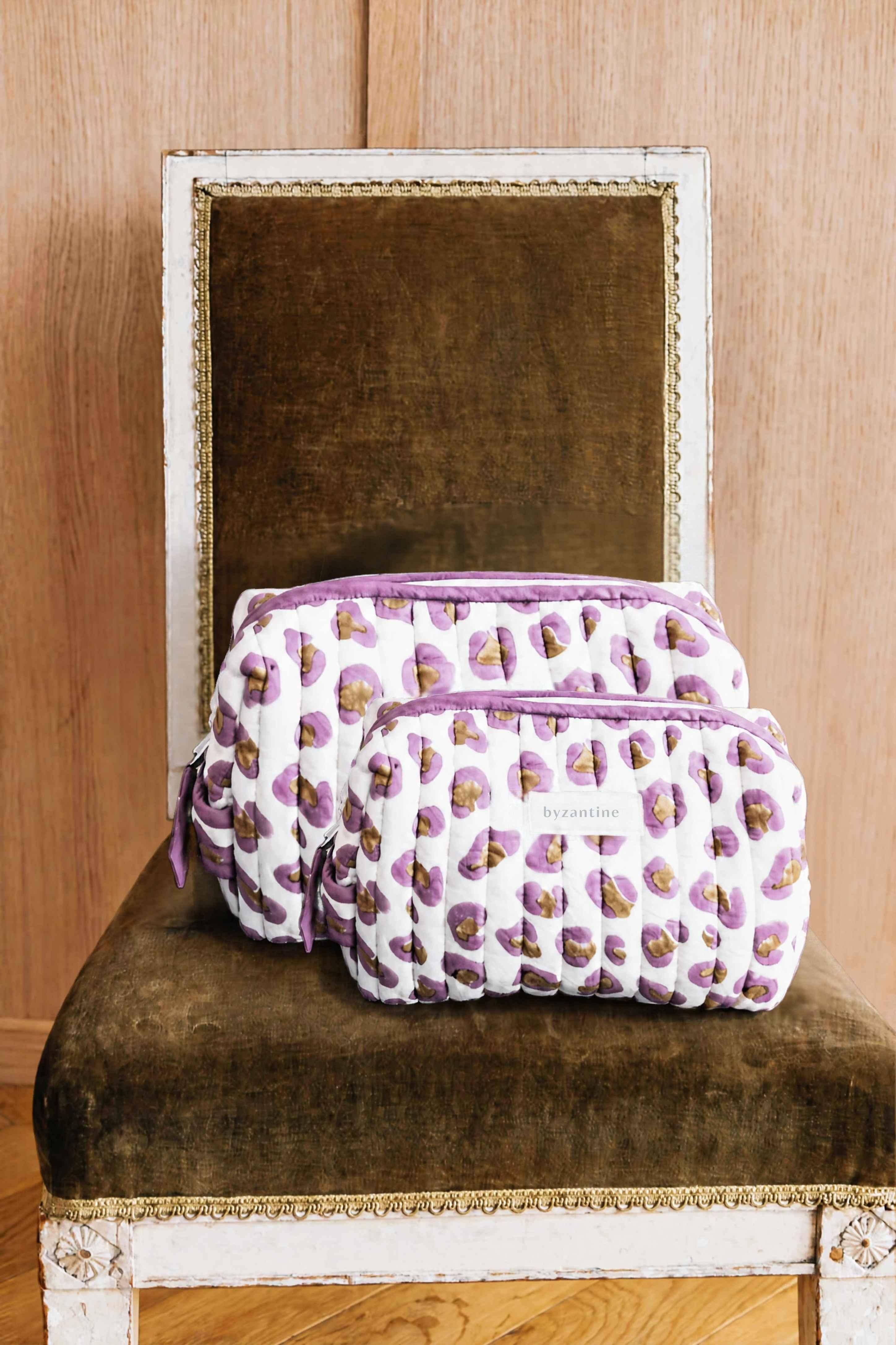 Duo de trousses de toilette Léopard Écru et Violet de byzantine posées sur une chaise en velours