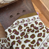 Foulard 60x60 Léopard Écru et Kaki de byzantine posé sur un tabouret en bois