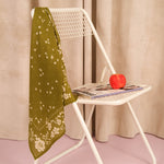 Foulard Antonia Kaki en voile de coton posé sur une chaise blanche, avec une pomme