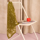 Foulard Antonia Kaki en voile de coton posé sur une chaise blanche, avec une pomme