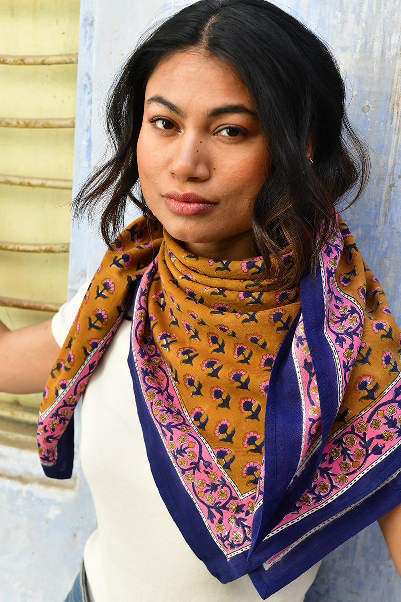 Grand foulard Séléné Fauve porté noué au cou, petits bouquets roses sur fond fauve, bordure bleue