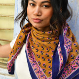 Grand foulard Séléné Fauve porté noué au cou, petits bouquets roses sur fond fauve, bordure bleue