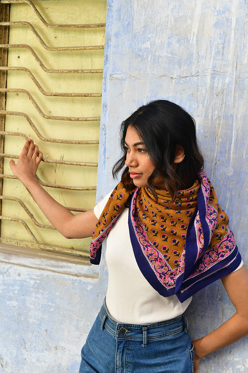 Grand foulard Séléné Fauve porté sur les épaules devant un mur bleu, bordure rose et bleu roi
