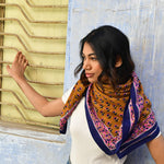Grand foulard Séléné Fauve porté sur les épaules devant un mur bleu, bordure rose et bleu roi