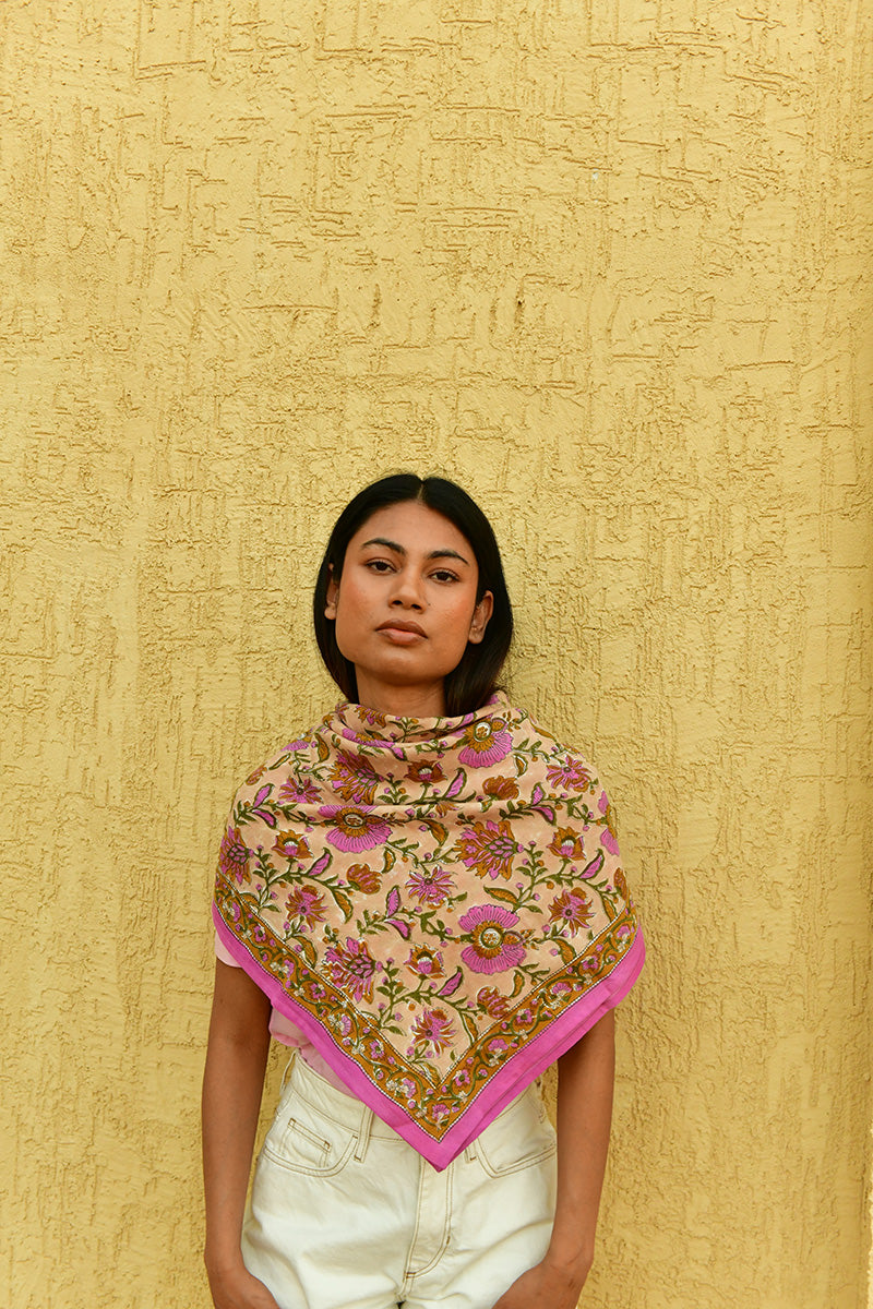 Grand foulard Théodora Rose porté en triangle devant un mur jaune