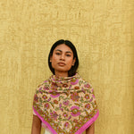 Grand foulard Théodora Rose porté en triangle devant un mur jaune