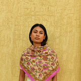 Grand foulard Théodora Rose porté en triangle devant un mur jaune