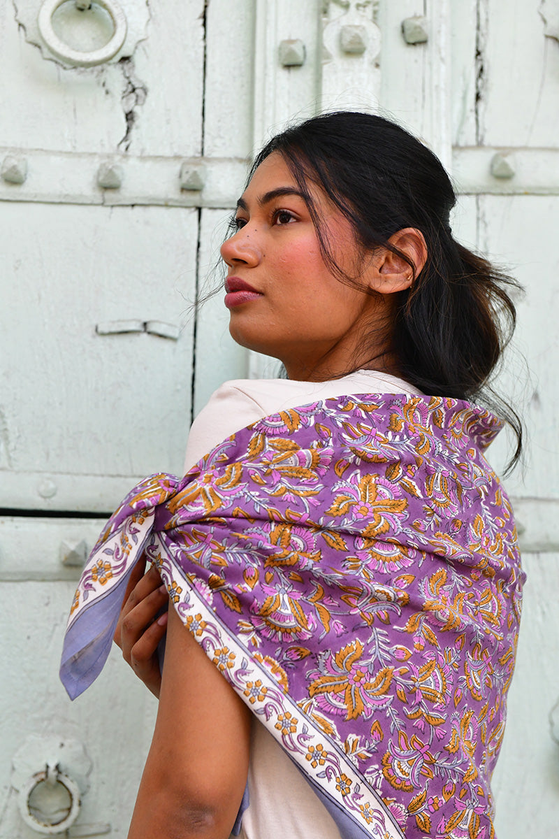 Grand foulard Totila Prune de byzantine porté sur l'épaule devant une porte blanche