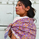Grand foulard Totila Prune de byzantine porté sur l'épaule devant une porte blanche