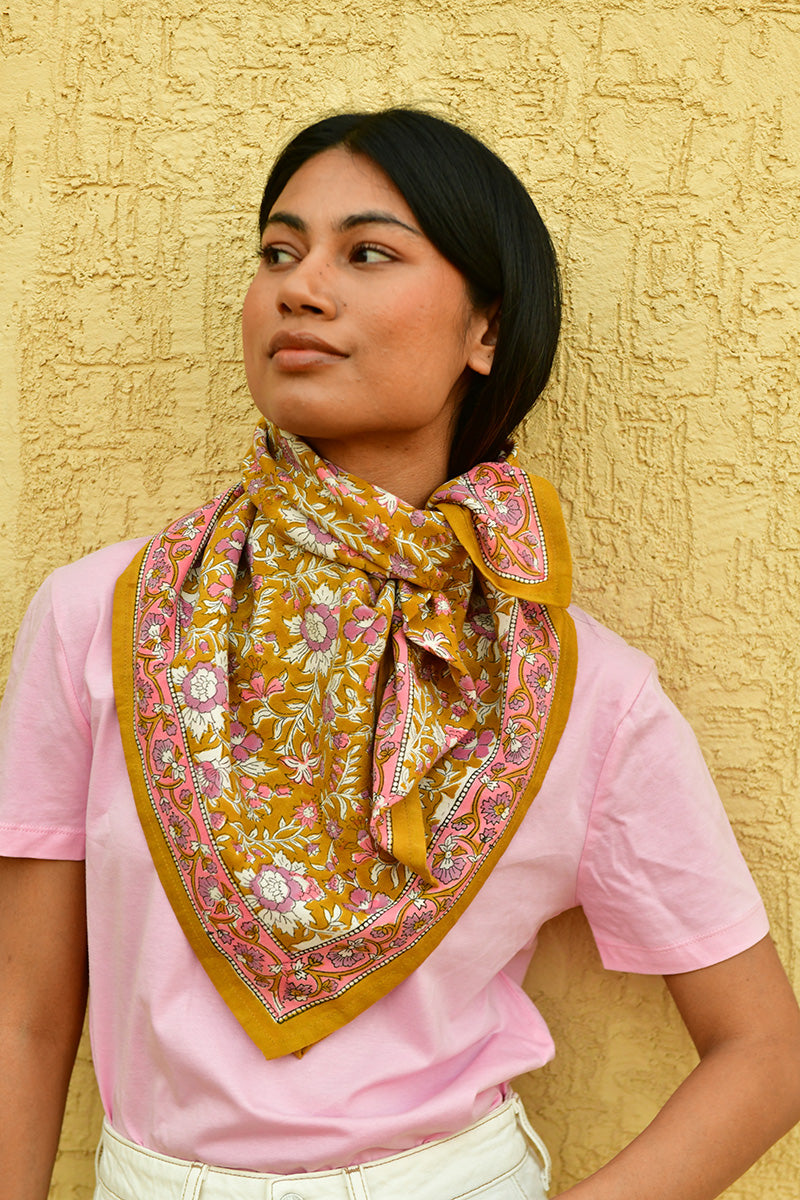 grand foulard calypso de byzantine en coton imprimé fleuri rose et violet sur fond marron clair caramel, porté par jeune femme autour du cou