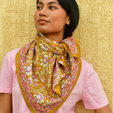 grand foulard calypso de byzantine en coton imprimé fleuri rose et violet sur fond marron clair caramel, porté par jeune femme autour du cou