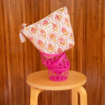 Grande trousse beauté Éphèse Rose posée sur une corbeille rose, sur un tabouret