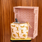 Grande trousse beauté Fauve Rose à nœud posée sur un tabouret, devant une caisse rose