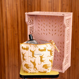 Grande trousse beauté Fauve Rose à nœud posée sur un tabouret, devant une caisse rose