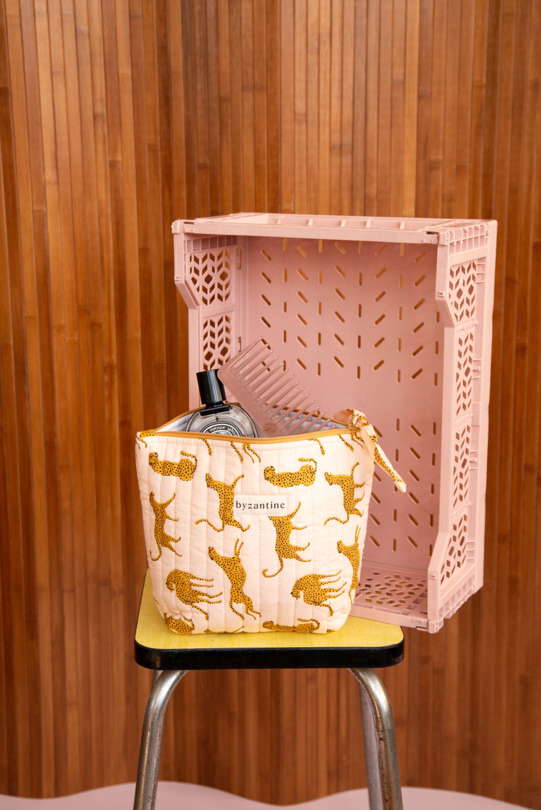 Grande trousse beauté Fauve Rose à nœud posée sur un tabouret, devant une caisse rose
