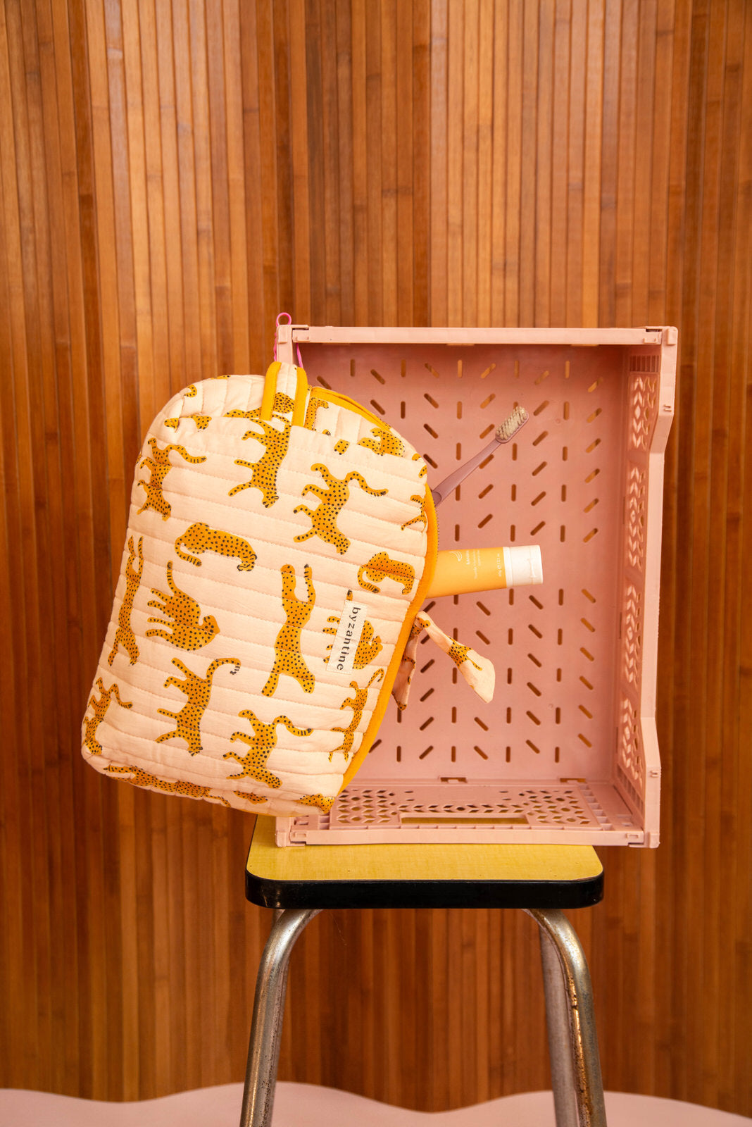 Grande trousse beauté Fauve Rose à zip moutarde posée contre une caisse rose
