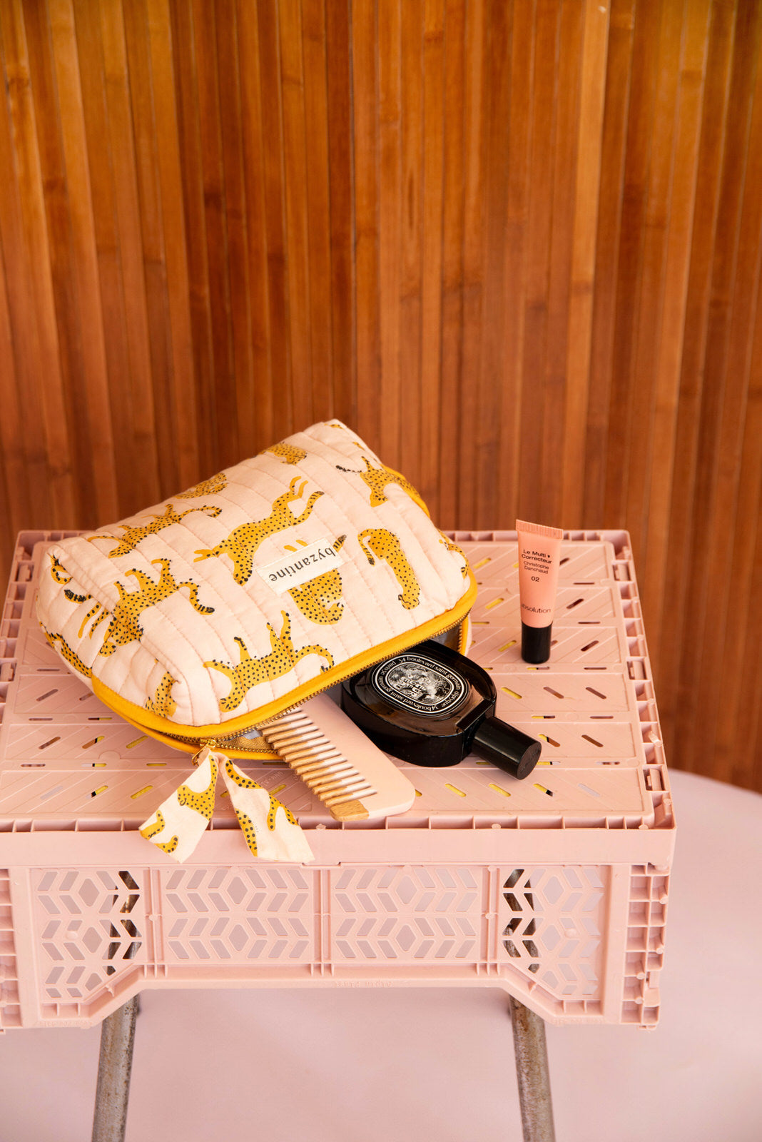 Grande trousse beauté Fauve Rose ouverte sur une caisse rose, avec peigne et parfum