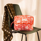 Grande trousse de toilette à rabat festonné Antioche Tomato de Byzantine posée sur une chaise verte