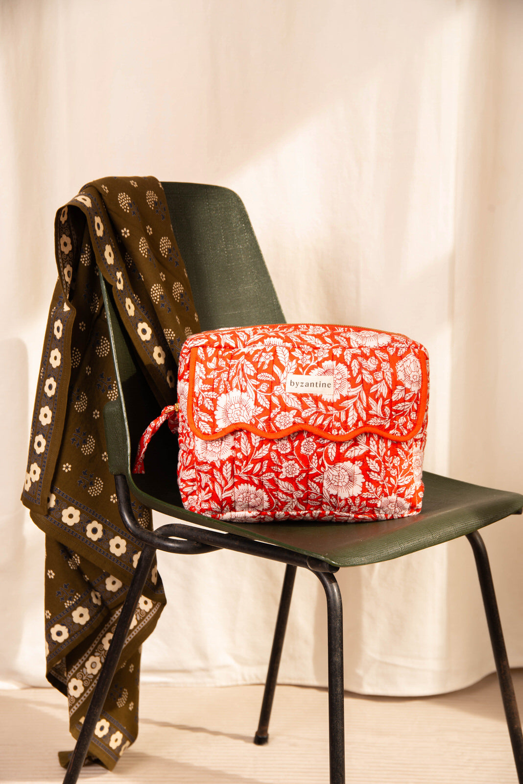 Grande trousse de toilette à rabat festonné Antioche Tomato de Byzantine posée sur une chaise verte