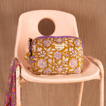 Grande trousse de toilette Carthage Kaki de Byzantine, passepoil violet, sur une chaise rose
