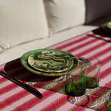 Nappe Byzantine rayée rose camélia dressée avec assiettes vertes et verres