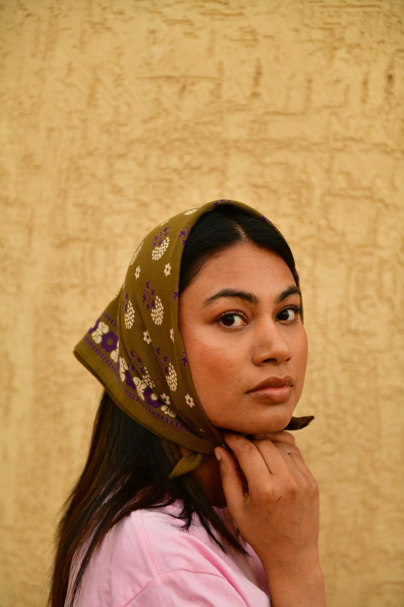 Petit foulard Anastase Olive porté en fichu sur la tête, main contre la joue
