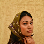Petit foulard Anastase Olive porté en fichu sur la tête, main contre la joue