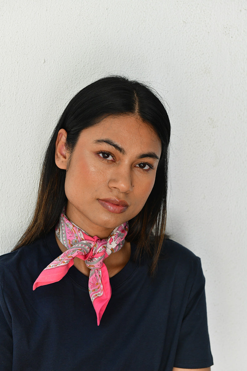 Petit foulard Andromaque Rose noué au cou, jeune femme devant un mur blanc