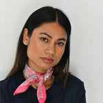 Petit foulard Andromaque Rose noué au cou, jeune femme devant un mur blanc