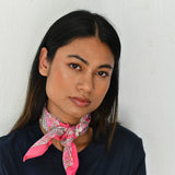 Petit foulard Andromaque Rose noué au cou, jeune femme devant un mur blanc