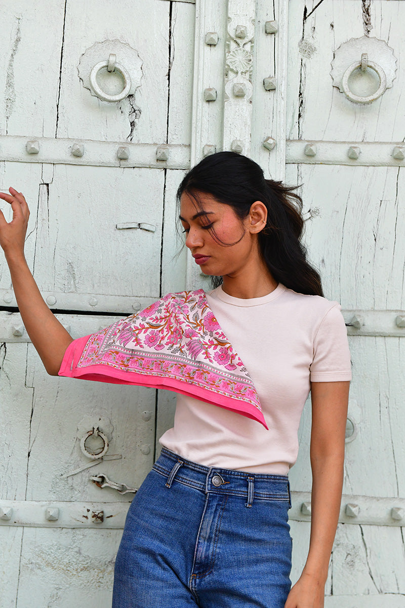 Petit foulard Andromaque Rose porté sur l'épaule, devant une porte blanche